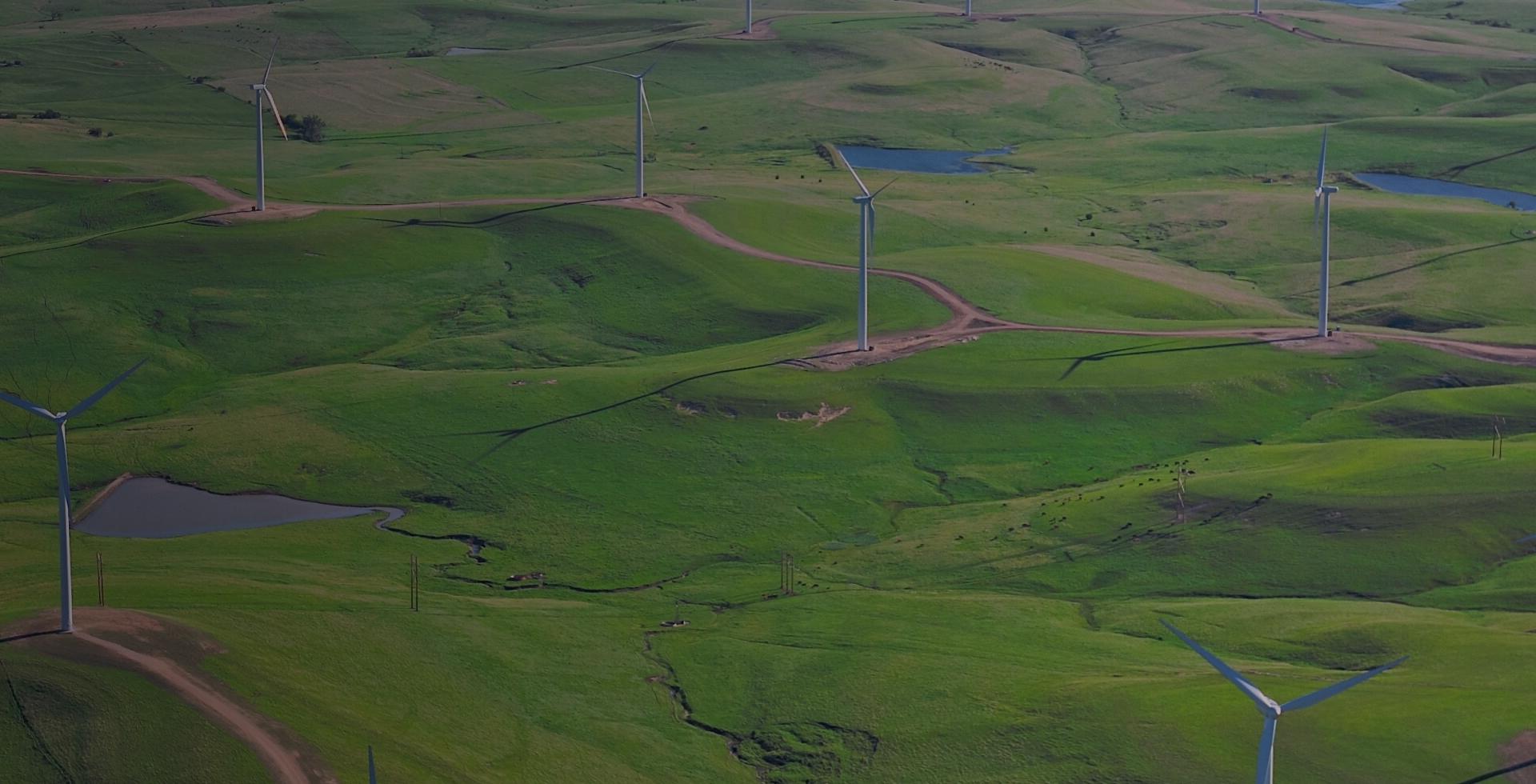 A wind turbine stands tall in a landscape of rolling green hills.